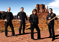 three male musicians and female singer in black attire standing in desert